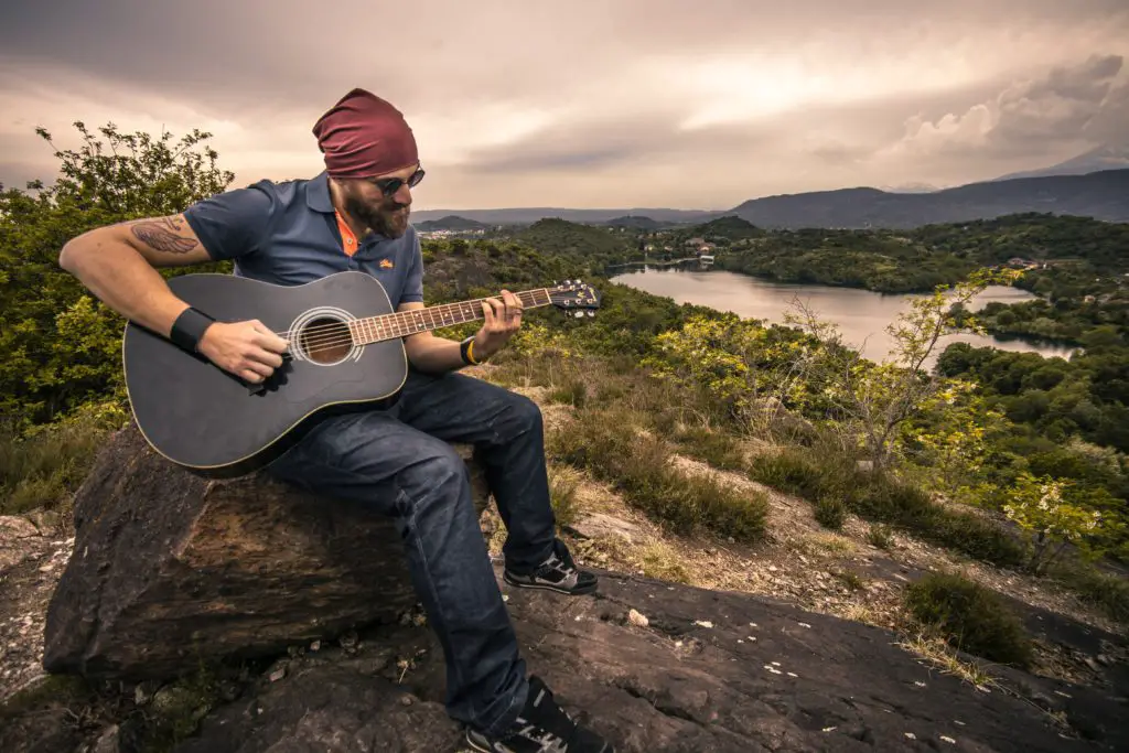 Man playing guitar outside sitting on a rock